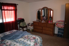 A bedroom with a bed, dresser and chair.