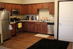 A kitchen with wood cabinets and black rug.