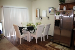 A dining room table with white chairs and a refrigerator.